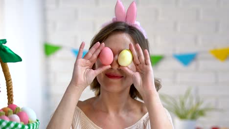 Beautiful-lady-playing-with-dyed-Easter-eggs-holding-them-near-eyes-festive-mood