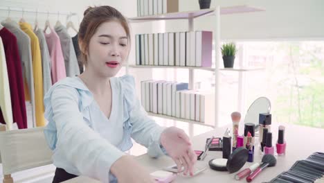 Beauty-Blogger-präsentieren-Kosmetik-Schönheit-sitzen-vor-Kamera-für-Videoaufnahmen.-Schöne-asiatische-Frau-verwenden-Kosmetika-während-Beitrag-Make-up-Tutorial-live-Video-mit-sozialen-Netzwerk-über-das-Internet-übertragen.