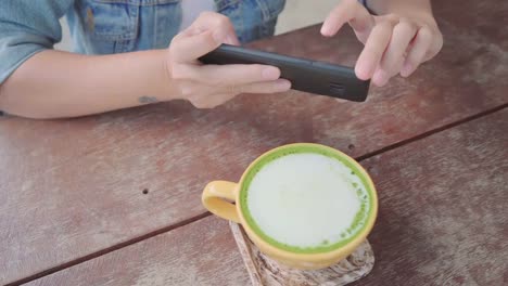 Female-blogger-photographing-green-tea-cup-in-cafe-with-her-phone.-A-young-woman-taking-photo-of-coffee-tea-on-smartphone,-photographing-meal-with-mobile-camera.