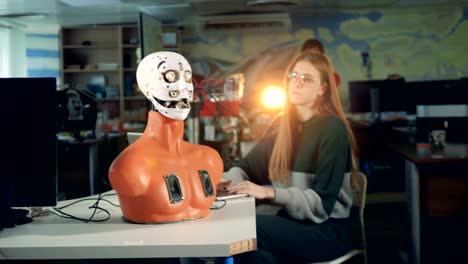 Young-girl-controls-a-robot-on-a-table.-Futuristic-humanoid-and-engineer.