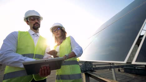 Two-workers-check-solar-panels,-standing-on-a-roof,-close-up.