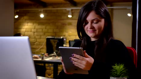 Closeup-portrait-of-adult-caucasian-businesswoman-scrolling-down-the-web-on-the-tablet-and-smiling-sitting-in-front-of-the-laptop