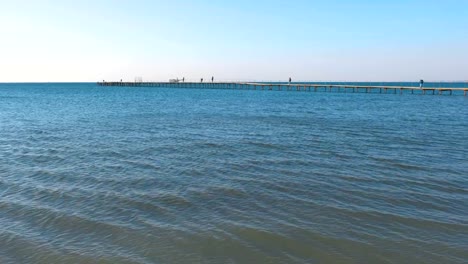 People-are-walking-on-old-wooden-pier-in-the-sea.-Side-view.