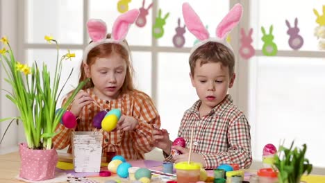 Glückliche-Kinder,-die-am-Ostersamstag-hanzige-Ohren-tragen-und-Eier-malen.-Kleine-Mädchen-bereiten-sich-auf-das-Osterfest-vor.