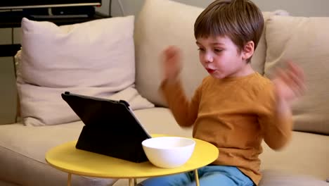 Kind-mit-Tablett-PC-auf-Bett-zu-Hause.-Niedlicher-Junge-auf-dem-Sofa-ist-zu-beobachten-Cartoon,-spielen-Spiele-und-lernen-von-Laptop.-Bildung,-Spaß,-Freizeit,-Glück,-moderne-Computertechnik-und-Kommunikation.