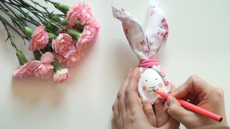 Women's-and-children's-hands-hold-chicken-egg-decorated-for-Easter-bunny,-paint-rabbit's-face-with-pink-marker.