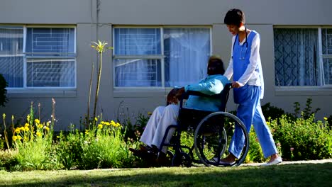 Side-view-of-Caucasian-female-doctor-pushing-senior-patient-in-wheelchair-at-nursing-home-4k