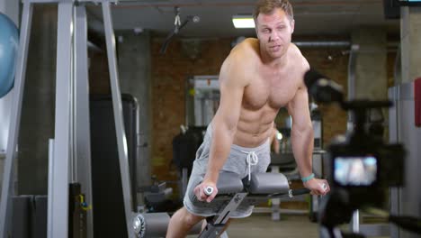 Entrenador-hablando-en-cámara-y-mostrando-el-aumento-de-tronco-en-gimnasio-Bench