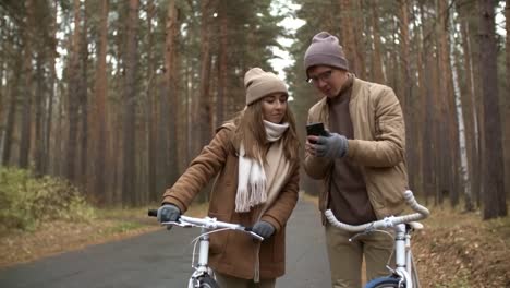 Pareja-discutiendo-mapa-en-Smartphone-mientras-está-de-pie-con-bicicletas-en-Park