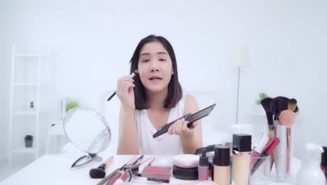 Beauty-Blogger-präsentieren-Beauty-Kosmetik-sitzen-vor-der-Kamera-für-die-Aufnahme-von-Video.-Glücklich-schöne-junge-asiatische-Frau-verwenden-Kosmetik-Rezension-Make-up-Tutorial-übertragen-Live-Video-an-soziale-Netzwerk.