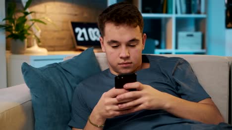 Ein-hübscher-Teenager,-der-mit-einem-Freund-über-soziale-Medien-auf-seinem-Smartphone-unterwegs-ist,-während-er-auf-einer-Couch-sitzt