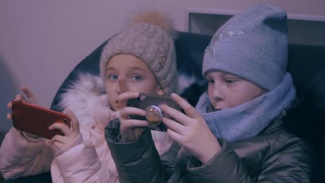 Two-teenager-girls-in-winter-clothes-watching-mobile-phones-and-playing-in-game