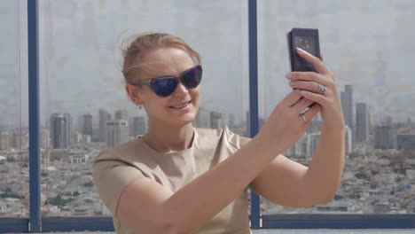 Smiling-woman-making-cell-photo-against-Tel-Aviv-view-from-the-height