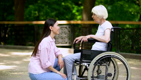 Lächelnde-Freiwillige-im-Gespräch-mit-alten-Frauen-im-Rollstuhl,-behinderten-Menschen-unterstützen