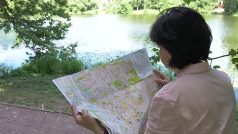 Morena-mira-un-mapa-de-papel-en-el-parque-cerca-del-estanque