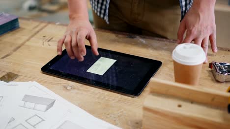 Close-up-of-male-hand-touching-tablet-screen-in-wood-workshop-indoors