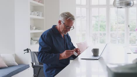 Senior-Man-In-Wheelchair-At-Home-Suchen-sie-Informationen-über-Medikamente-online-mit-Laptop