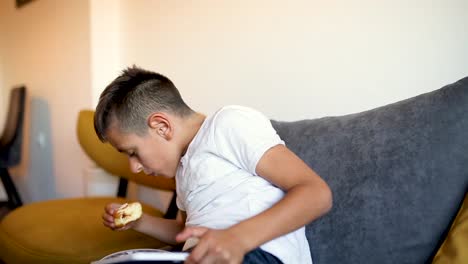 Joven-está-jugando-juegos-en-la-tableta-y-comer-rosquilla