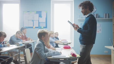 Lehrer-verwendet-digitalen-Tablet-Computer-während-erklärenin-einer-Lektion-zu-einem-Klassenzimmer-voller-verschiedener-Kinder,-in-der-Grundschule-Gruppe-von-intelligenten-multiethnischen-Kindern-lernen-Wissenschaft-und-kreatives-Denken