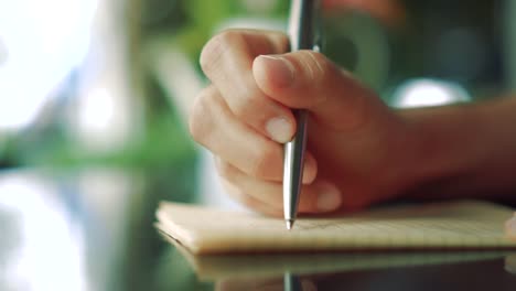 4K-espacio-de-copia-de-vídeo-de-la-mano-del-hombre-escribiendo-en-cuaderno-blanco-con-luz-bokeh-en-el-fondo-del-café.