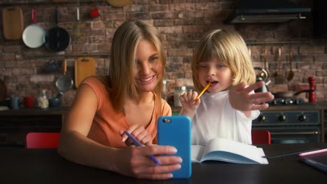 Mutter-und-Sohn-genießen-Online-Videoanruf-auf-dem-Smartphone,-während-Hausaufgaben-in-der-Schule-Copybook.-Sie-sitzen-in-der-Küche-am-Tisch.-Nahaufnahme