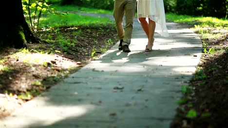 Male-and-female-legs-walking-on-a-path-in-forest-close-up.-Man-and-woman-stepping-onto-sun-lighted-spots-in-spring-park-shallow-depth-of-field.-Togetherness-dating-flirting-marriage-love-story-concept