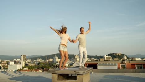 CLOSE-UP:-Girl-and-boy-holding-hands-and-jumping-on-rooftop-above-the-city