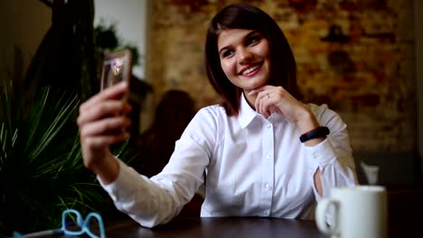 A-beautiful-girl-sits-in-a-cafe-and-after-drunk-a-hot-coffe,-poses-for-a-mobile-phone-camera-to-make-a-beautiful-self-for-social-networks