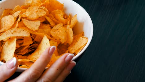 Großer-Teller-mit-Kartoffel-Chips-auf-dem-Tisch.-Weibliche-Hände-mit-schönen-Maniküre-nehmen-chips