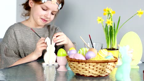 Happy-easter.-A-sweet-curly-girl-is-preparing-for-the-celebration-of-Easter.-She-paints-the-wooden-figure-of-a-rabbit-with-paints