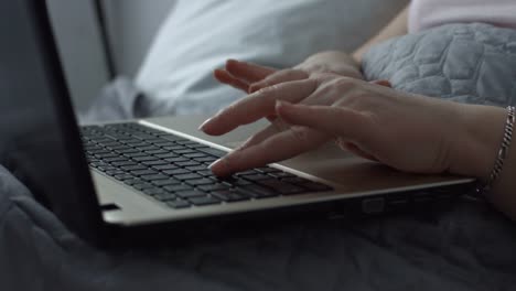 Female-hands-typing-on-laptop-keyboard-in-the-bed