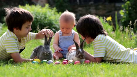 Niños-lindos,-hermanos-niño,-niño-y-preescolar,-jugando-con-conejitos-y-huevos-de-Pascua-en-una-primavera-floreciente-jardín.-Niño-juega-con-el-conejo,-caza-para-vacaciones-del-huevo