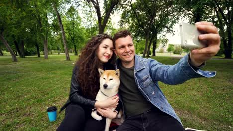 Fröhlicher-Kerl-nimmt-Selfie-holding-Smartphone-und-seine-Frau-zu-küssen,-während-sie-entzückenden-Hund-hält-und-küssen.-Beziehung,-Liebe,-Romantik-und-Technologie-Konzept.