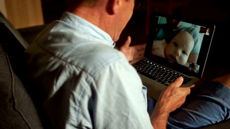 A-mature-man-talks-to-his-adult-son-and-newborn-grandson-on-Skype.-Video-communication,-three-generations-of-one-family