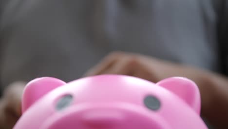 Hand-putting-coins-in-a-pink-piggy-bank,-saving-money-concept