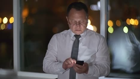 Asian-White-Collar-Worker-Using-Smartphone-in-Dark-Office