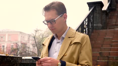 Closeup-of-attractive-caucasian-male-typing-on-the-phone-calmly-standing-in-the-park-outdoors