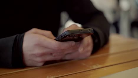 Male-hands-using-smartphone-above-wooden-table