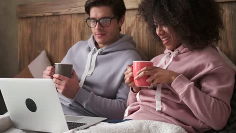 Pareja-tomando-café-y-uso-portátil-en-la-cama