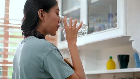 Young-asian-woman-drinking-water-and-using-tablet.-technology,-social-network,-communication-concept-in-kitchen-at-home.