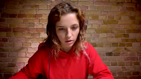 Close-up-portrait-of-young-blogger-in-headphones-in-front-of-camera-reading-and-talking-on-bricken-wall-background.