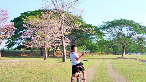 An-Asian-woman-jogging-in-natural-sunlight-in-the-evening,-along-with-his-son-riding-a-bicycle.--exercising-for-good-health.-Slow-Motion