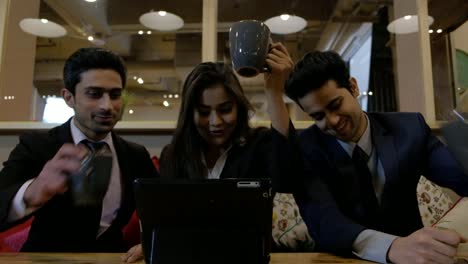 Handheld-shot-of-coworkers-colleagues-huddled-together-at-cafe-table-as-they-stare-at-laptop-screen-coming-up-with-solution-they-cheers-with-their-mugs-together-to-celebrate-and-congratulate