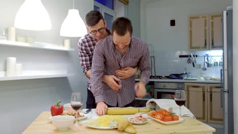 Couple-of-men-gay-roll-out-the-pizza-dough-together-hugging.