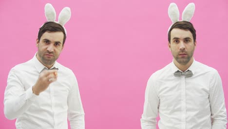 Young-handsome-boy-standing-on-a-pink-background.-A-man-with-rabble-ears-on-his-head.-A-man-holding-a-carrot-puts-it-in-his-mouth-and-reproduces-the-movements-of-a-cigarette-with-a-cigarette-lighter.