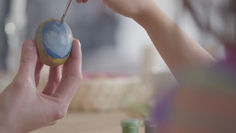 Close-up-of-mother-and-daughter-hands-coloring-easter-eggs-with-colors-and-brush.