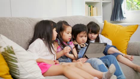 Gruppe-von-Kindern,-die-mit-digitalem-Tablet-zusammen-auf-dem-Sofa-zu-Hause-spielen,-und-lächelnd,-Kinder-auf-digitalem-Tablet-im-Wohnzimmer.