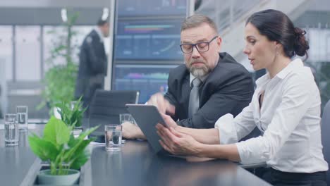 En-la-sala-de-reuniones-ejecutivo-femenino-muestra-tableta-digital-de-ordenador-a-inversor-masculino,-que-discutir-estadísticas-y-el-potencial-de-inversión-de-empresas.-Oficina-Corporativa-ocupada-con-empresarios-que-trabajan