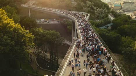 A-crowd-of-people-on-a-pedestrian-bridge-in-the-spring-evening.-Aerial-view.-A-new-bicycle-pedestrian-bridge-in-the-center-of-the-capital-of-Ukraine,-the-city-of-Kiev.-Excursions-and-walks-for-tourist