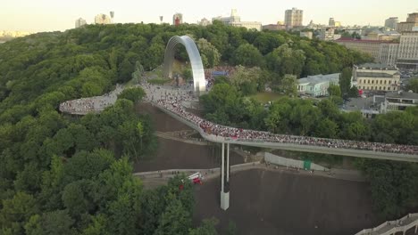 A-crowd-of-people-on-a-pedestrian-bridge-in-the-spring-evening.-Aerial-view.-A-new-bicycle-pedestrian-bridge-in-the-center-of-the-capital-of-Ukraine,-the-city-of-Kiev.-Excursions-and-walks-for-tourist